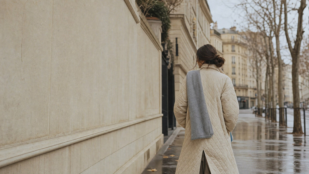 Woman in a long quilted coat walking a quiet city street on an autumn morning